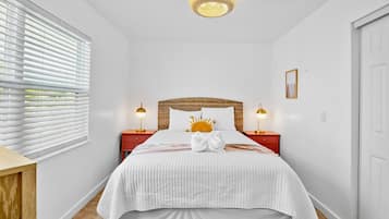 Un dormitorio con una cama, dos mesitas de noche, un aplique de pared y una ventana con persianas.