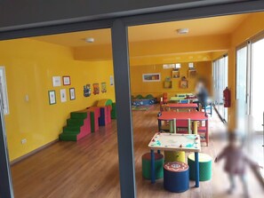 A brightly colored playroom with wooden flooring, colorful play structures, and tables with stools. - H1 - 1908 - Condominio Hispania (Lima)