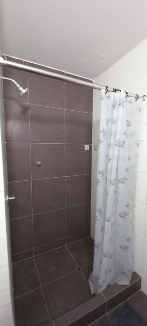 Un espace douche avec des carreaux de couleur foncée, une pomme de douche et un rideau à motifs.