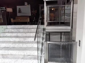 Eine Reihe von Marmorstufen führt zu einem modernen, mehrstöckigen Eingangsbereich mit Glastüren und einem Metallgeländer.