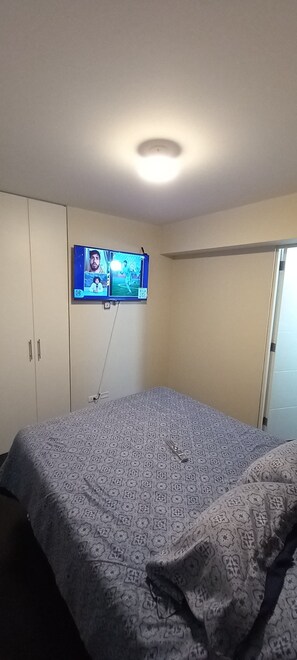 Une chambre à coucher avec un lit, un téléviseur fixé au mur et un luminaire au plafond.