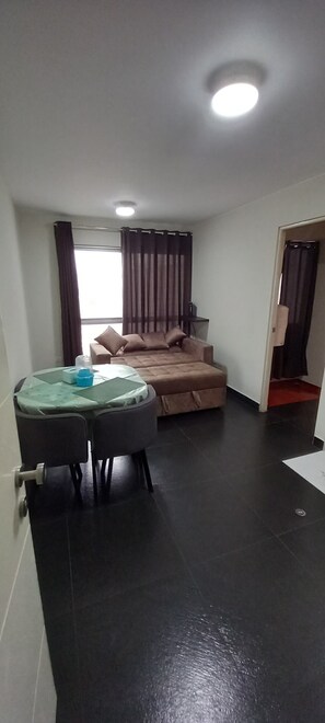 A compact room with a bed, a small table with chairs, and a window with curtains. - H1 - 1908 - Condominio Hispania (Lima)
