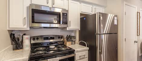 A kitchen with white cabinets, a stainless steel microwave, a refrigerator, and a stove.
