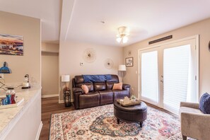 Ein Wohnzimmer mit einer Ledersofa, einem Couchtisch, einem gemusterten Teppich, einem Deckenventilator und einer Tür mit Fenster.