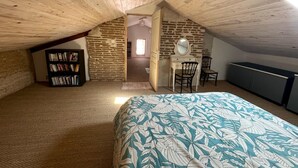 A cozy attic bedroom with a sloped ceiling, a bed with a leaf-patterned bedspread, a bookshelf, a desk with a mirror, and a dresser.