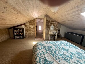 A cozy attic bedroom with a sloped ceiling, a bed with a leaf-patterned bedspread, a bookshelf, a desk with a mirror, and a dresser.