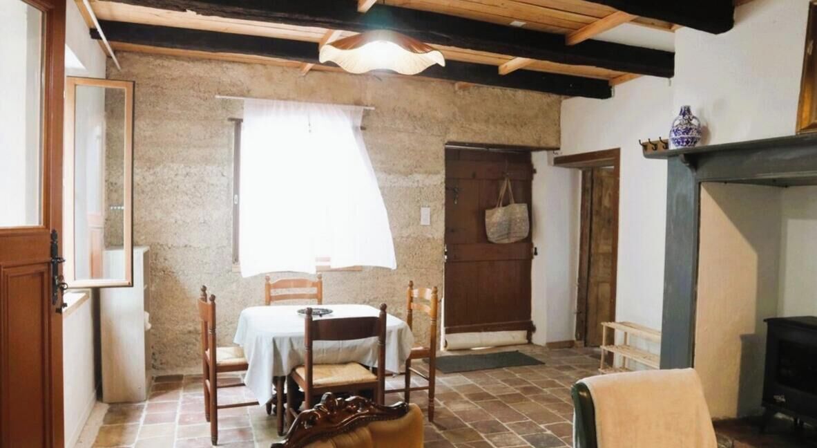 Ein rustikales Zimmer mit einer Steinwand, einem Holztisch mit Stühlen, einem Kamin und einer zur Außenwelt führenden Tür.