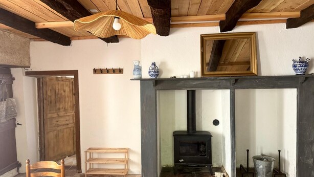 A rustic room with a fireplace, wooden beams, a bench, and a table.