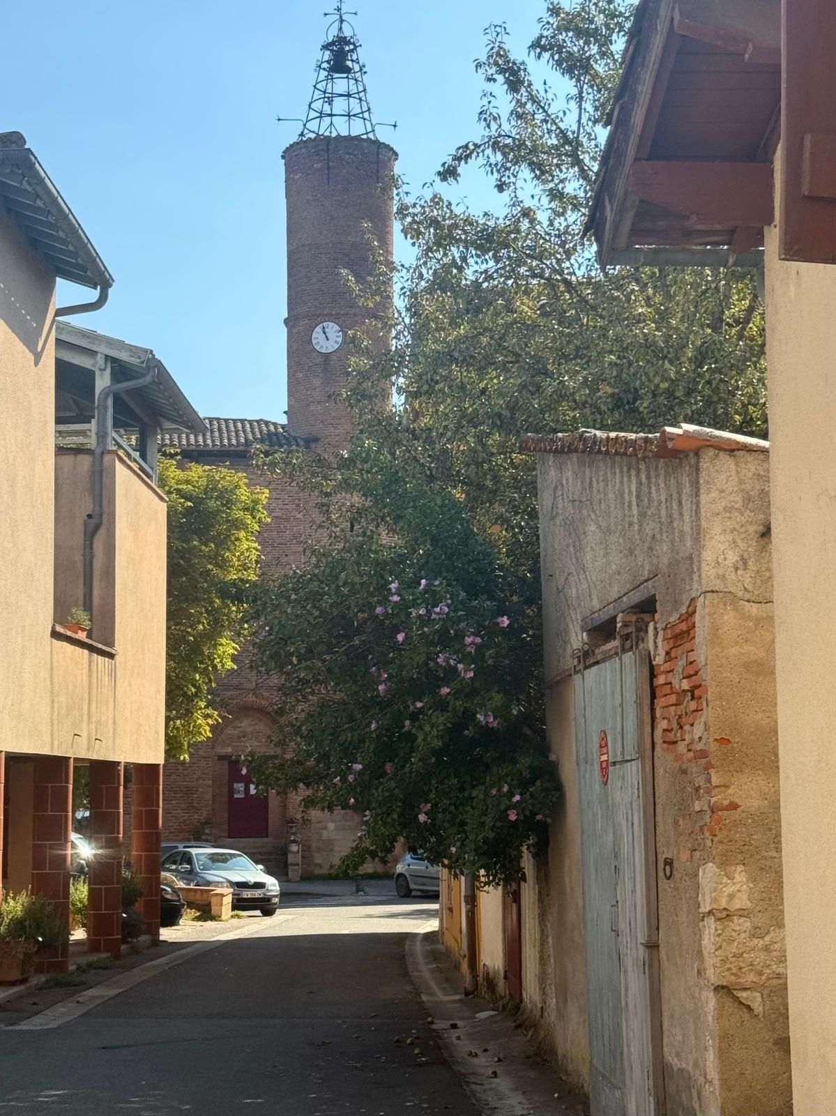 Eine enge Straße mit Gebäuden an beiden Seiten, ein Uhrturm im Hintergrund und ein Auto, das am Straßenrand geparkt ist.