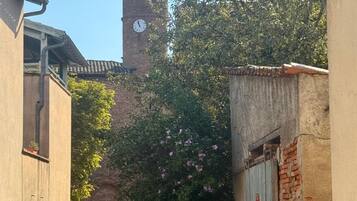 Eine enge Straße mit Gebäuden an beiden Seiten, ein Uhrturm im Hintergrund und ein Auto, das am Straßenrand geparkt ist.