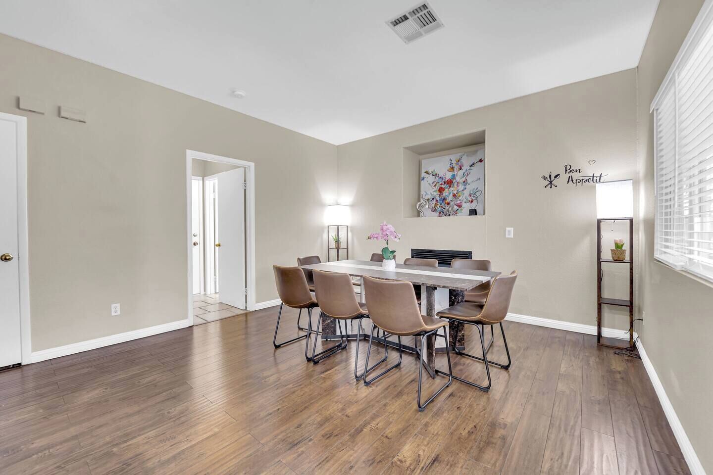 Un coin repas avec une table et des chaises, un tableau accroché au mur et une fenêtre avec des stores.