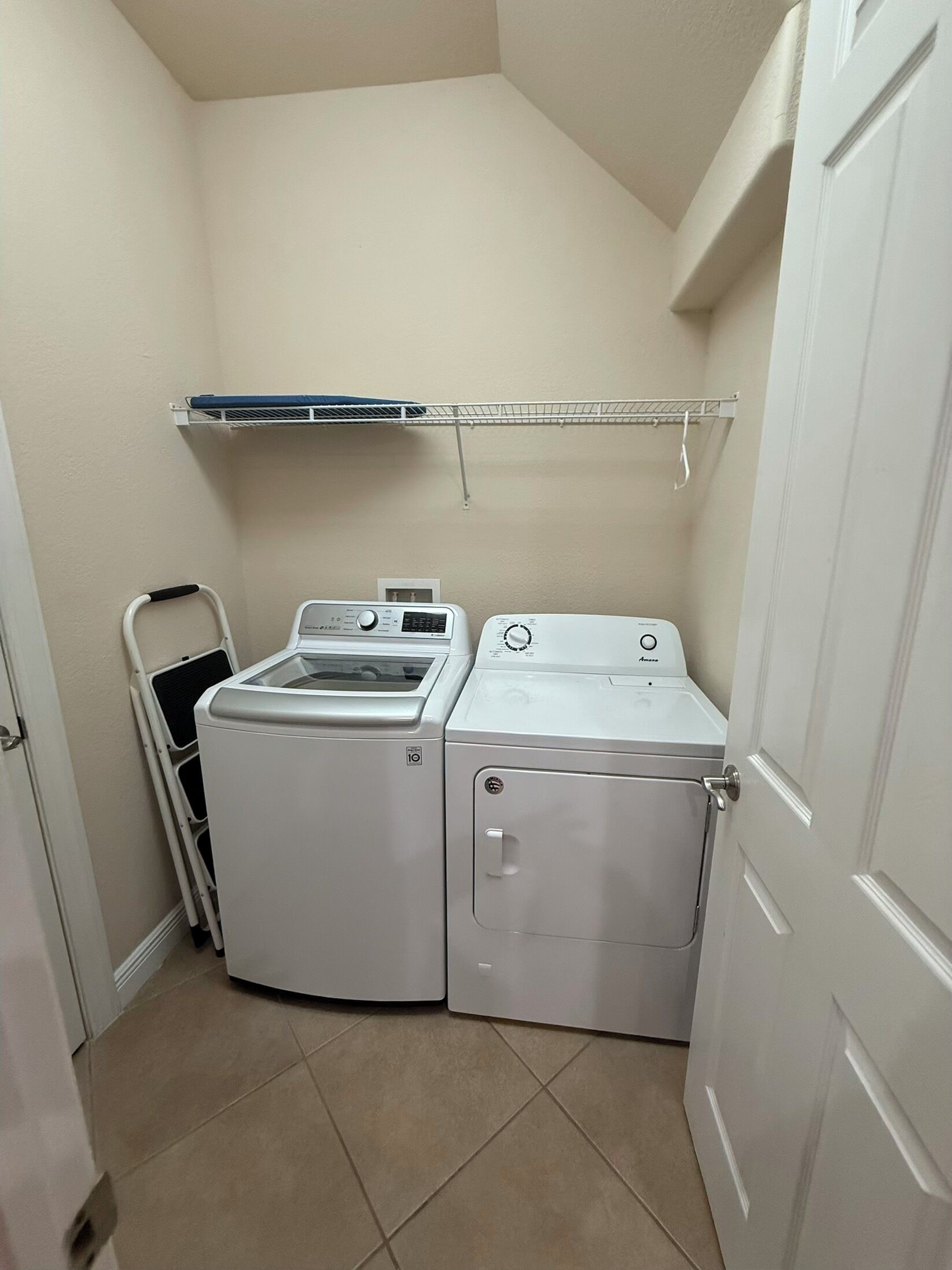 A laundry room with two white washing machines, a drying rack, and a folding chair.