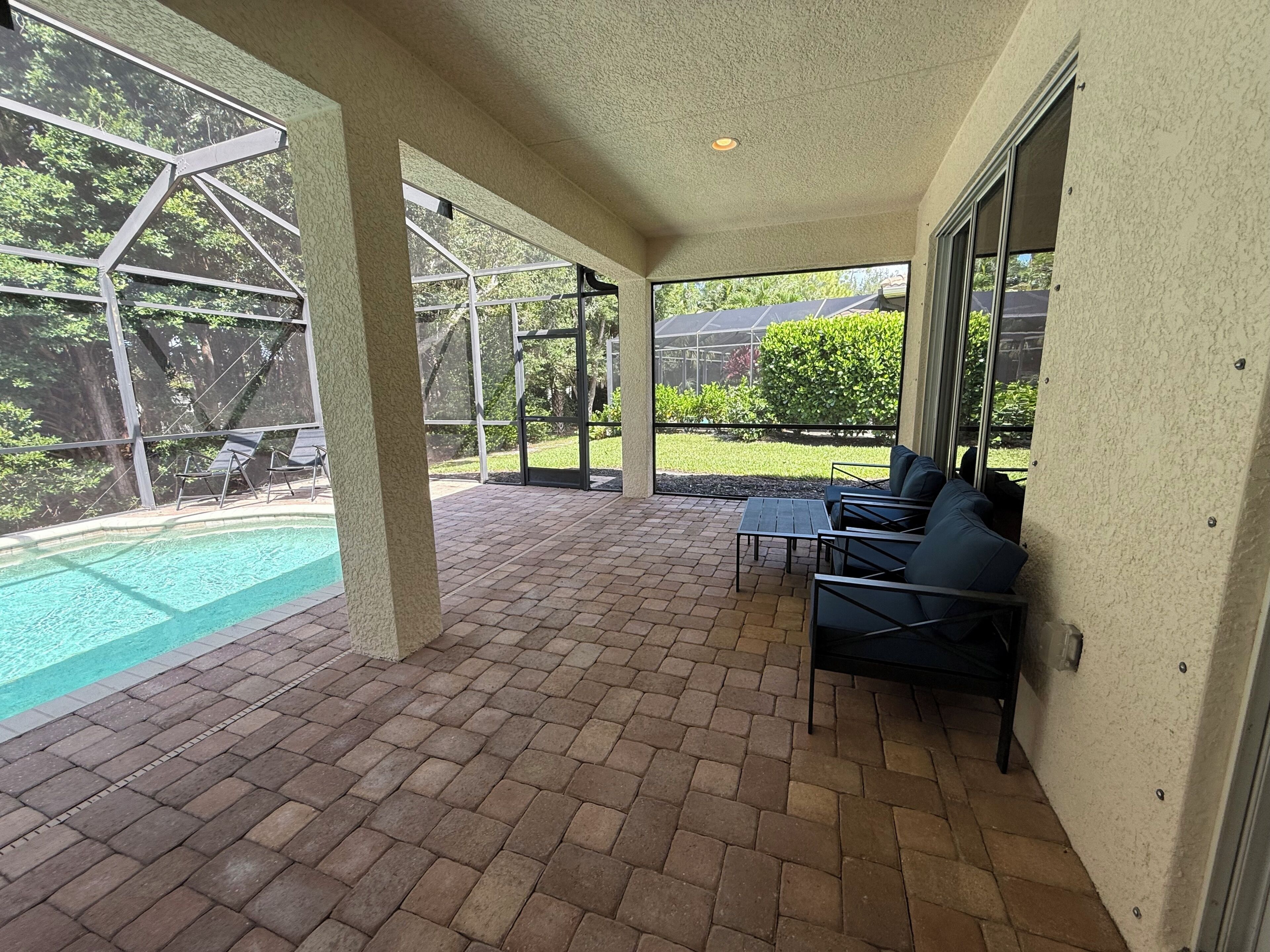 A covered patio area with a pool, outdoor seating, and a view of a garden.