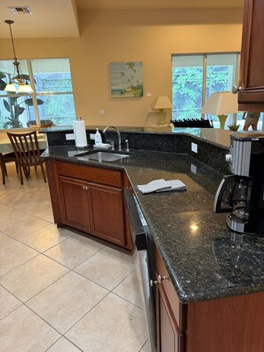 A kitchen with a granite countertop, wooden cabinets, a built-in dishwasher, and a window with a view of greenery. - Spacious 4-bedroom house in peaceful Naples perfect for families (Naples)