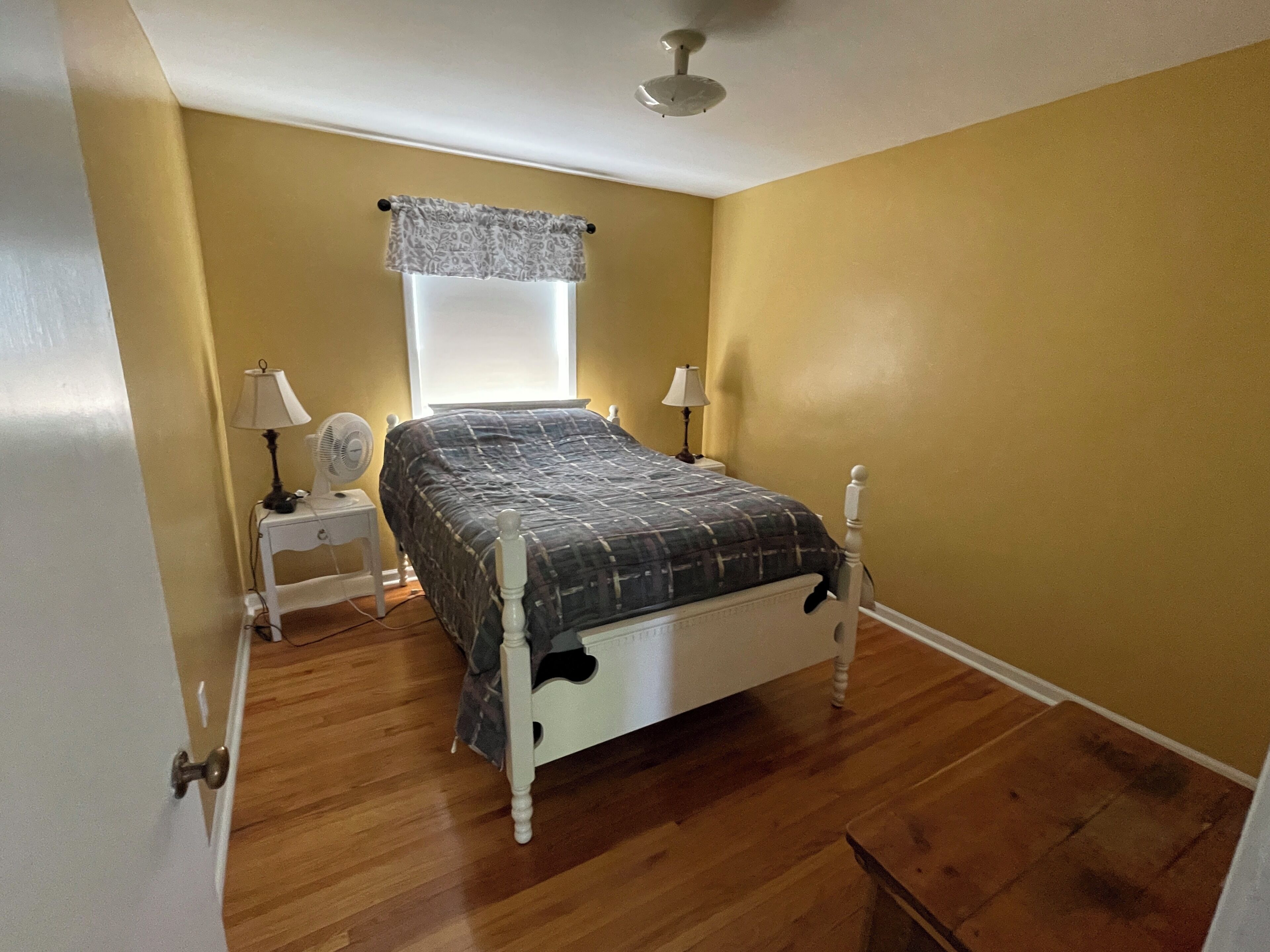 Quarto com cama, duas mesas de cabeceira com abajures, uma janela com cortina e um ventilador de teto.