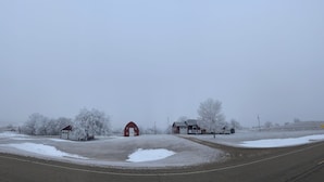 A rural landscape with snow-covered fields, a road, and several red barns.