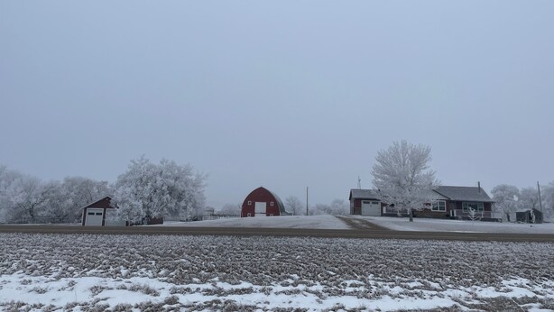 A rural landscape with a barn, a small house, and a field covered in snow.