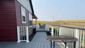 A wooden deck with a table and chairs, a white railing, and a view of a grassy field.