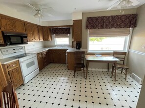 A kitchen with wooden cabinets, a microwave, an oven, a dining table with chairs, and a window with a view.