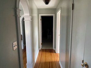 A hallway with a wooden floor, white walls, and a door leading to another room.