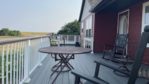 A wooden deck with a round table and chairs, a railing, and a view of a field.