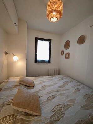 Un dormitori amb un llit, una làmpada penjada a la paret, una finestra i decoracions murals.