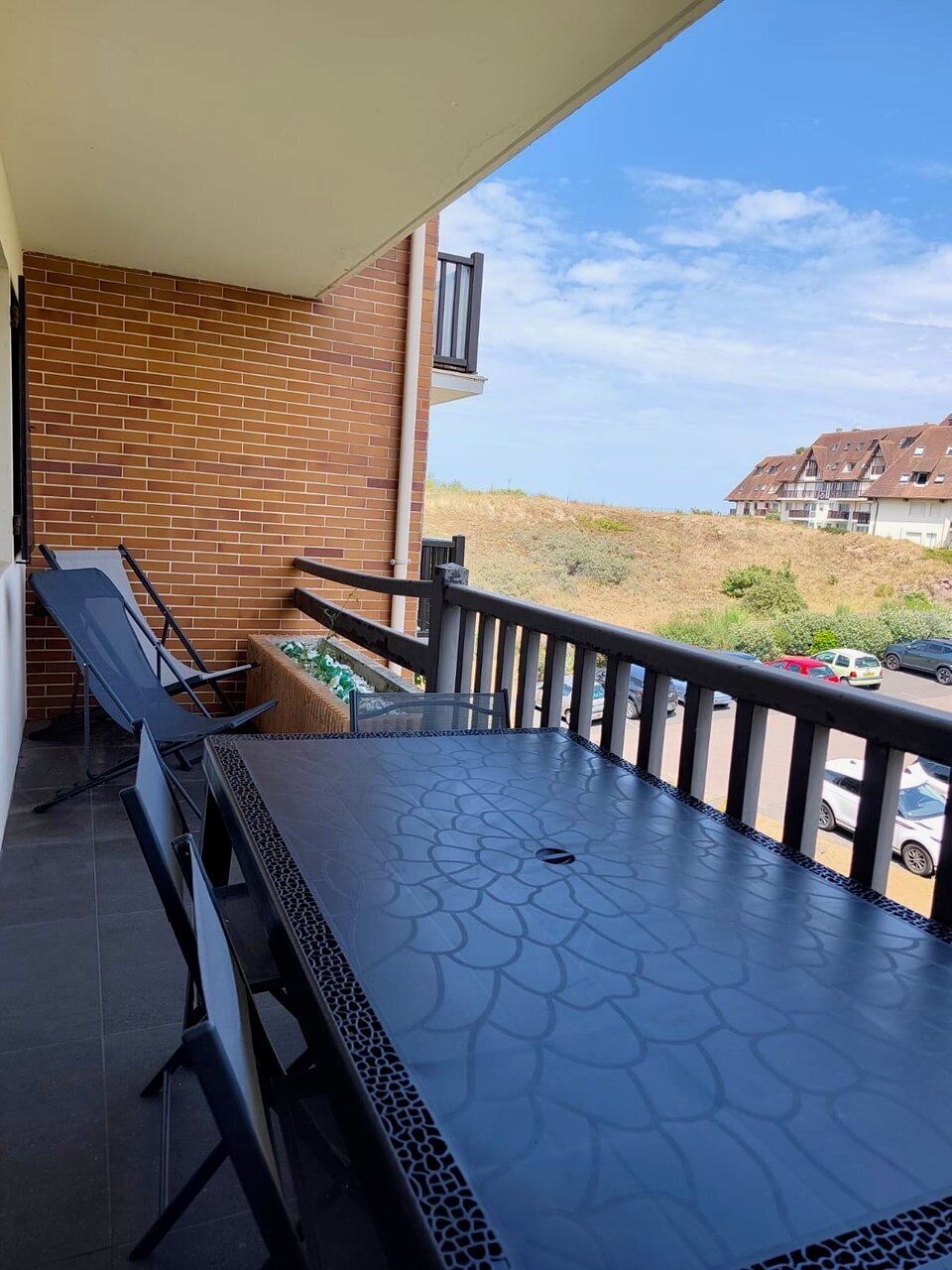 A balcony with a table and chairs, a brick wall, and a view of a residential area.