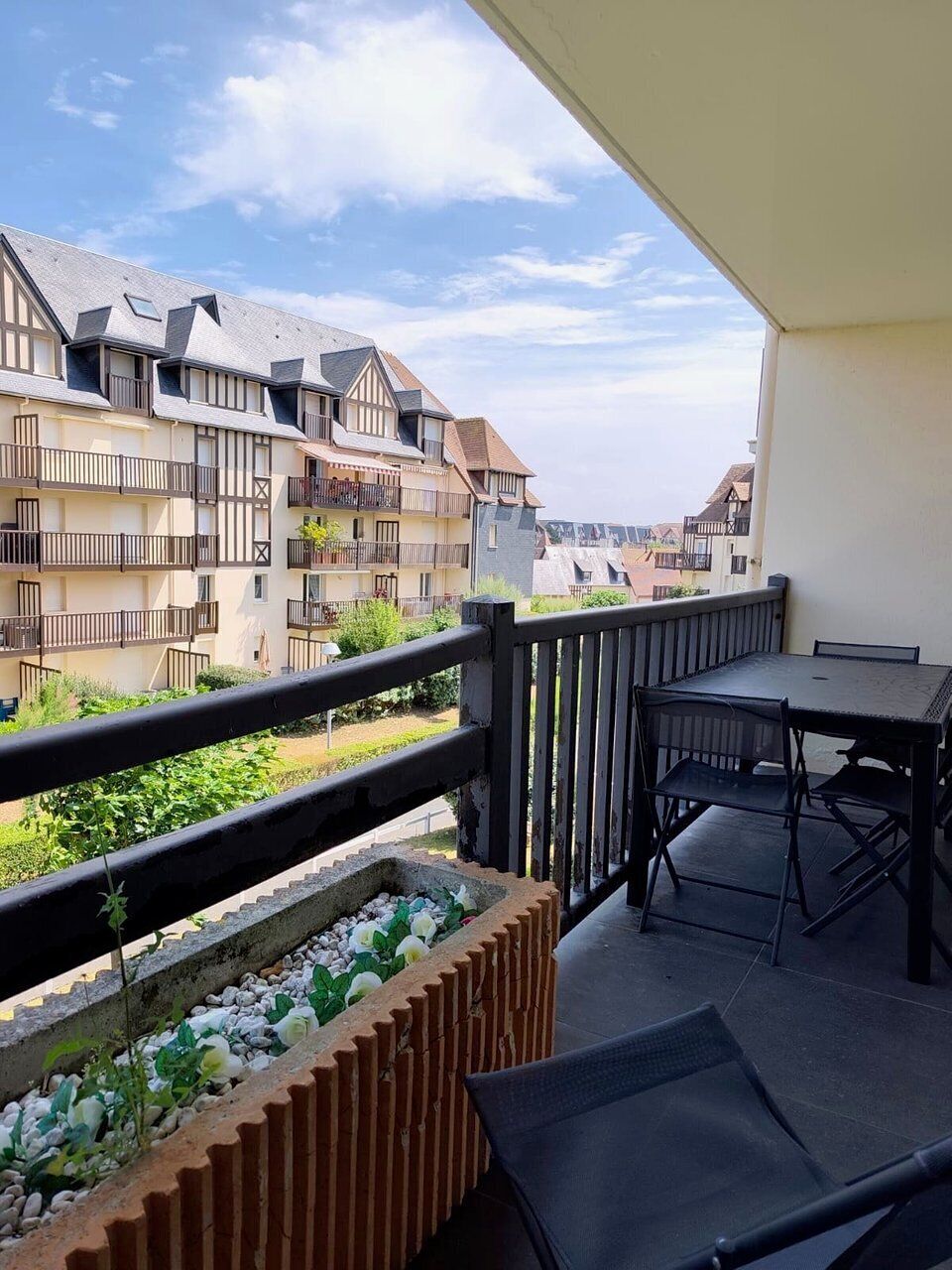 Ein Balkon mit Tisch und Stühlen, ein Blumenbeet und Blick auf benachbarte Gebäude.