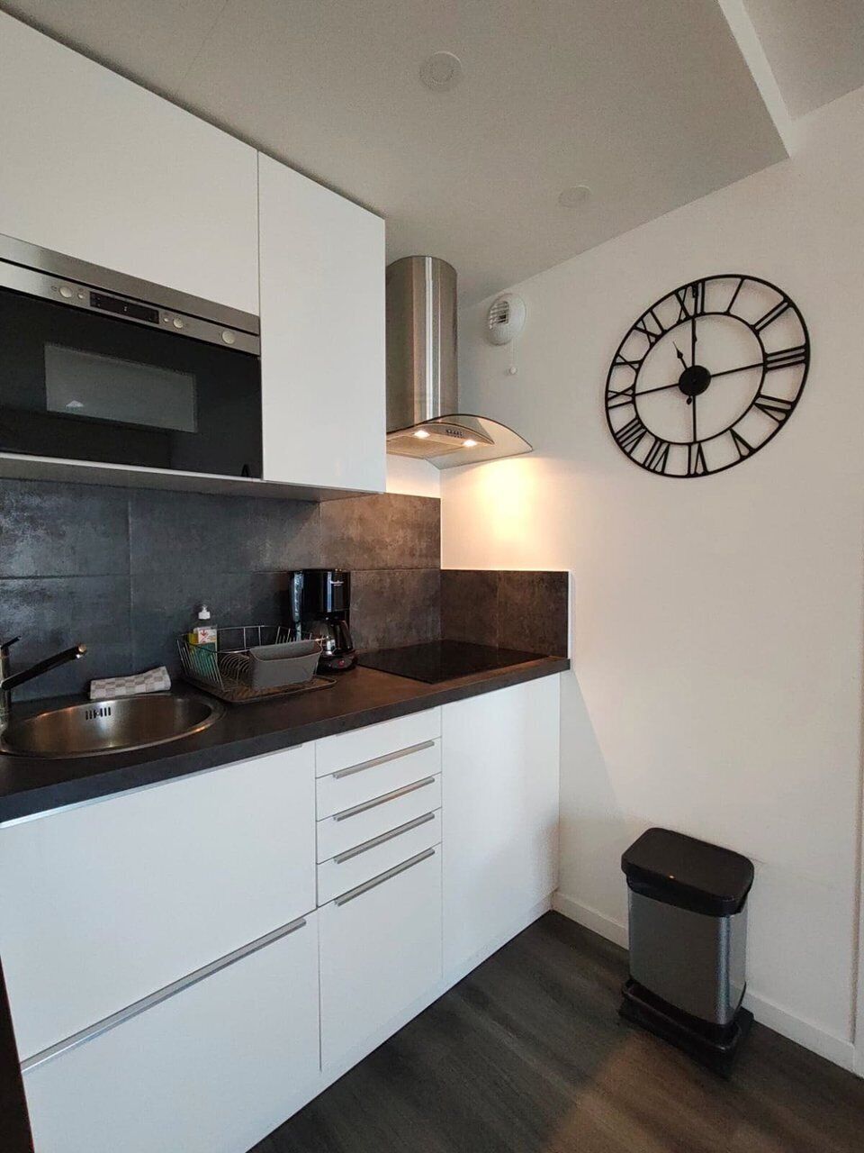 Una cocina moderna con armarios blancos, un lavamanos de acero inoxidable, una encimera negra y un reloj en la pared.
