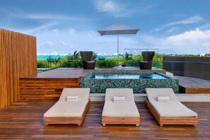 Eine Dachterrasse mit drei Liegestühlen, einem Whirlpool und einem großen Sonnenschirm.