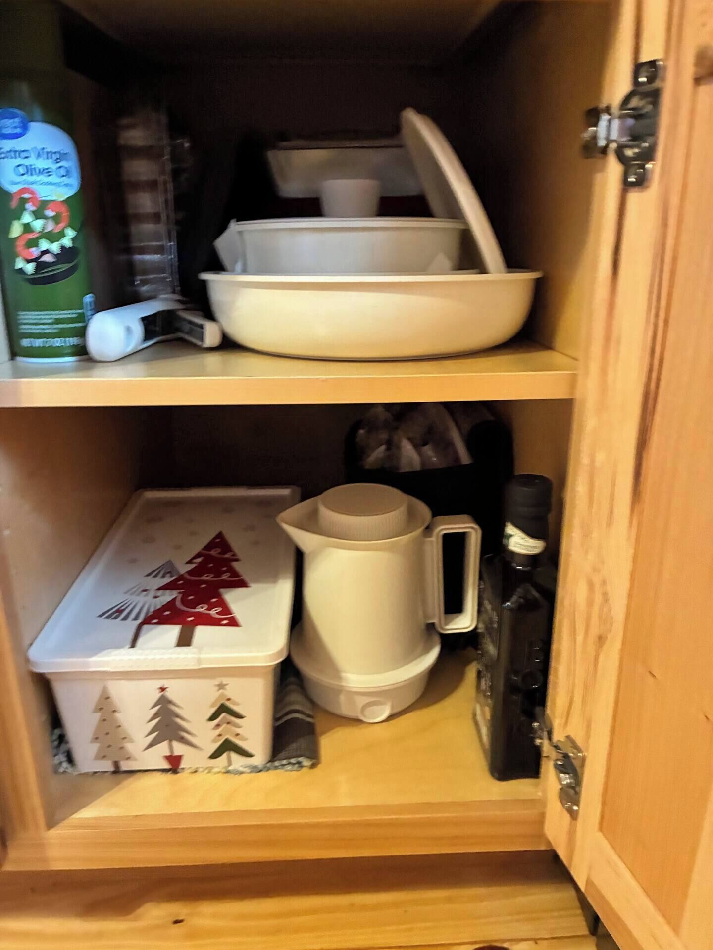 A wooden cabinet with shelves containing kitchenware, a container with a Christmas tree design, and a coffee maker.