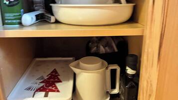 A wooden cabinet with shelves containing kitchenware, a container with a Christmas tree design, and a coffee maker.