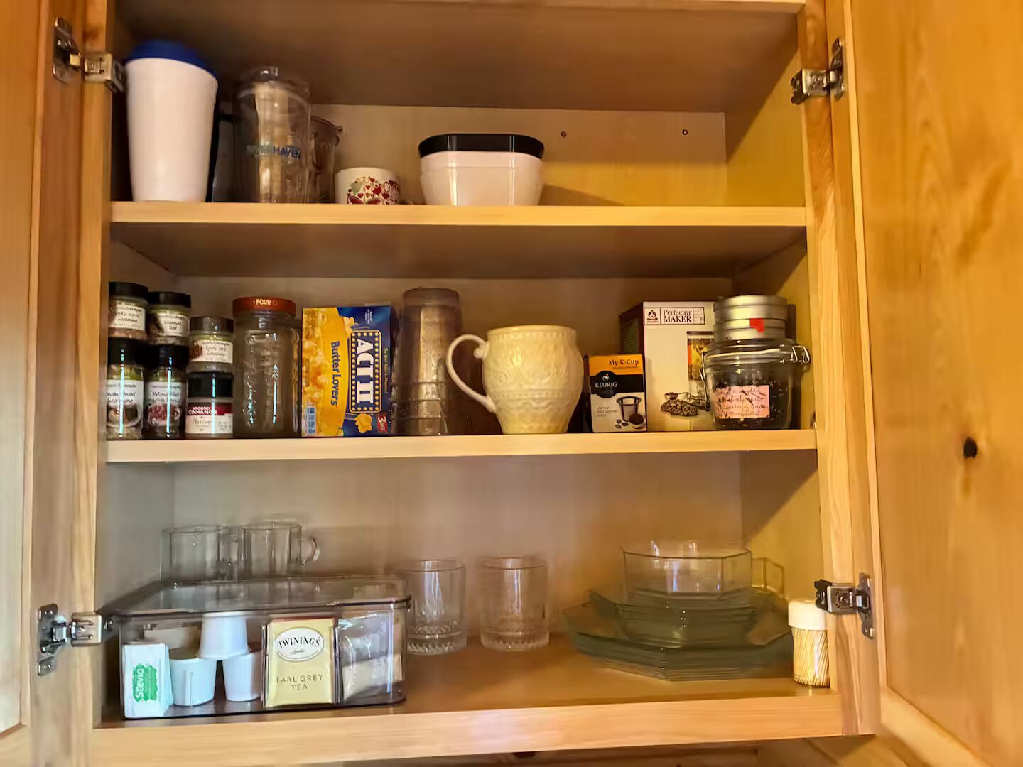 A kitchen cabinet with various food items and kitchenware.
