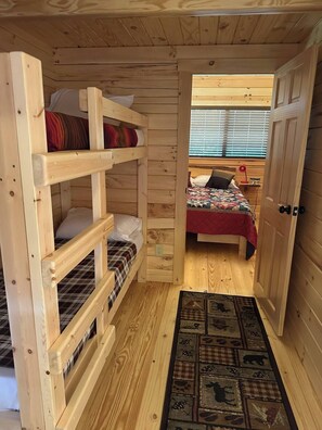 Eine Holzhütte mit Etagenbetten, einem Einzelbett mit einer Steppdecke und einer Tür zu einem anderen Raum.