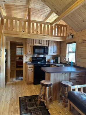 Interno di una baita in legno con cucina, zona pranzo e un angolo salotto accogliente.