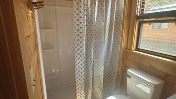 Ein kleines Badezimmer in einer Holzhütte mit Dusche, Toilette und einem Fenster.