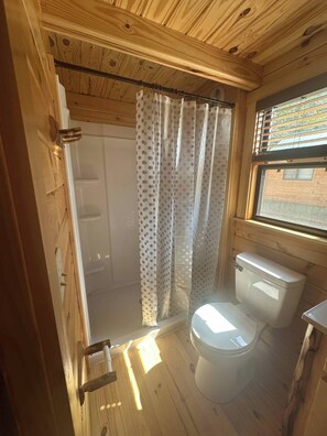 Ein kleines Badezimmer in einer Holzhütte mit Dusche, Toilette und einem Fenster.