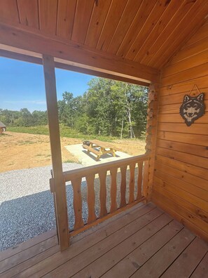 Eine Holzhütte mit Veranda, Picknicktisch und Blick auf ein bewaldetes Gebiet.