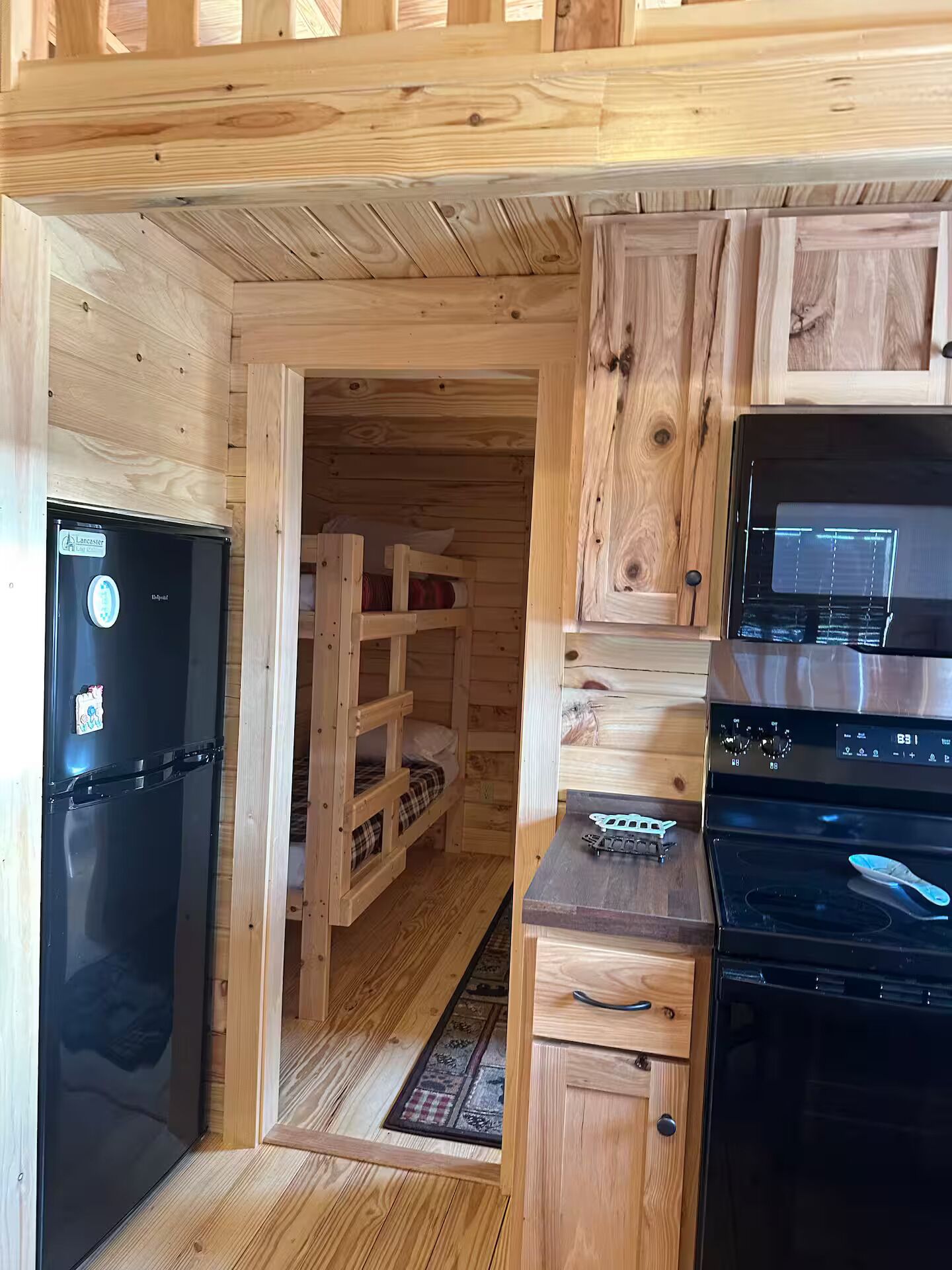A compact kitchen with wooden cabinetry, a black refrigerator, and a stove.