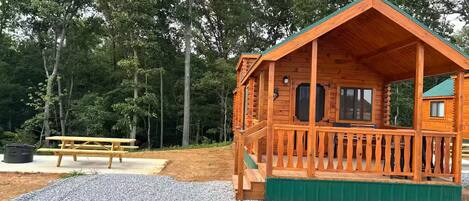 A wooden cabin with a porch, a picnic table, and a gravel area.