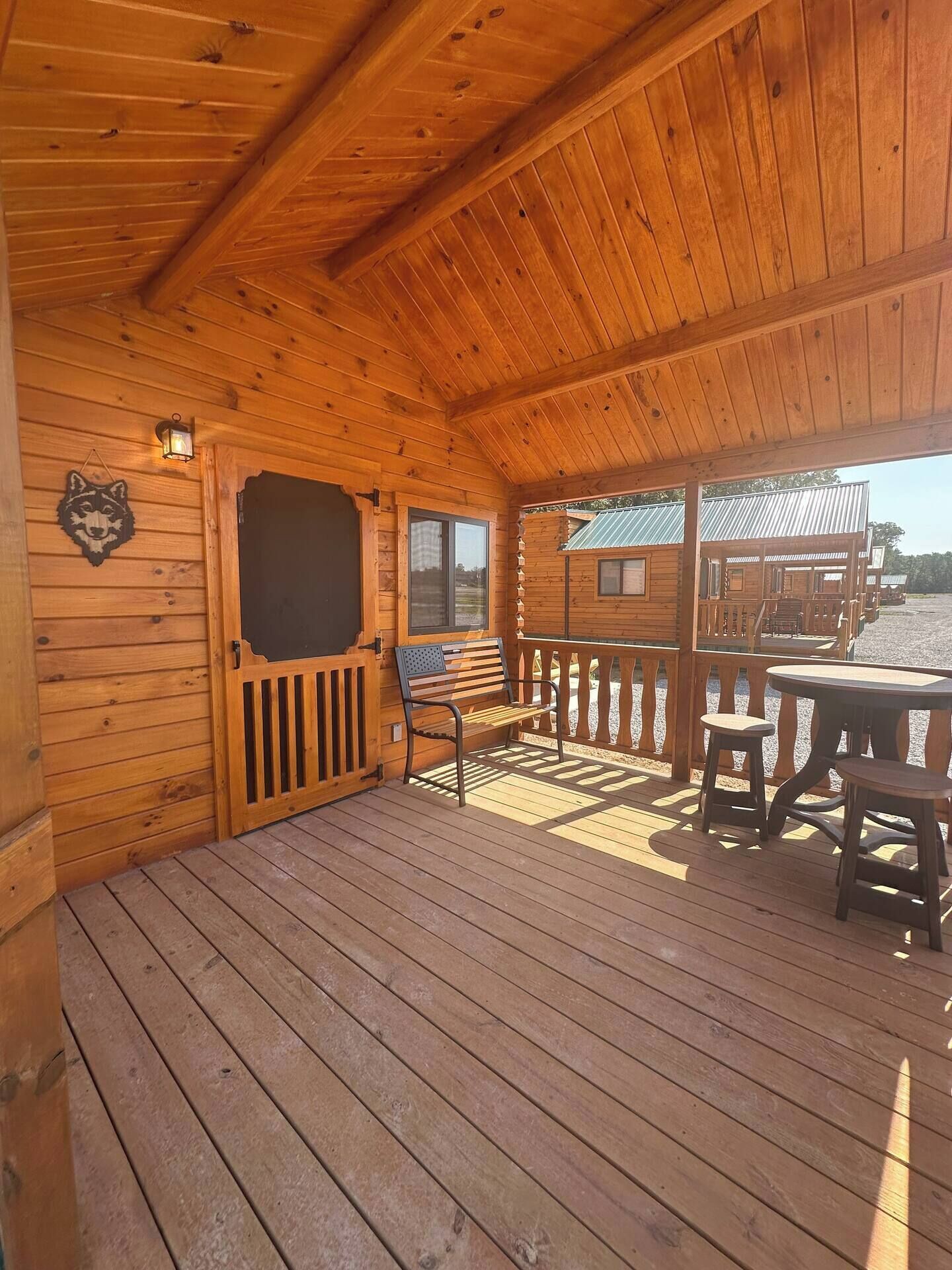 A wooden deck with a bench and table, a door with a window, and a cabin in the background.
