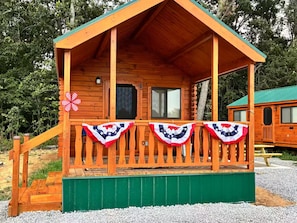 A wooden cabin with a porch, a green awning, and a flag decoration.