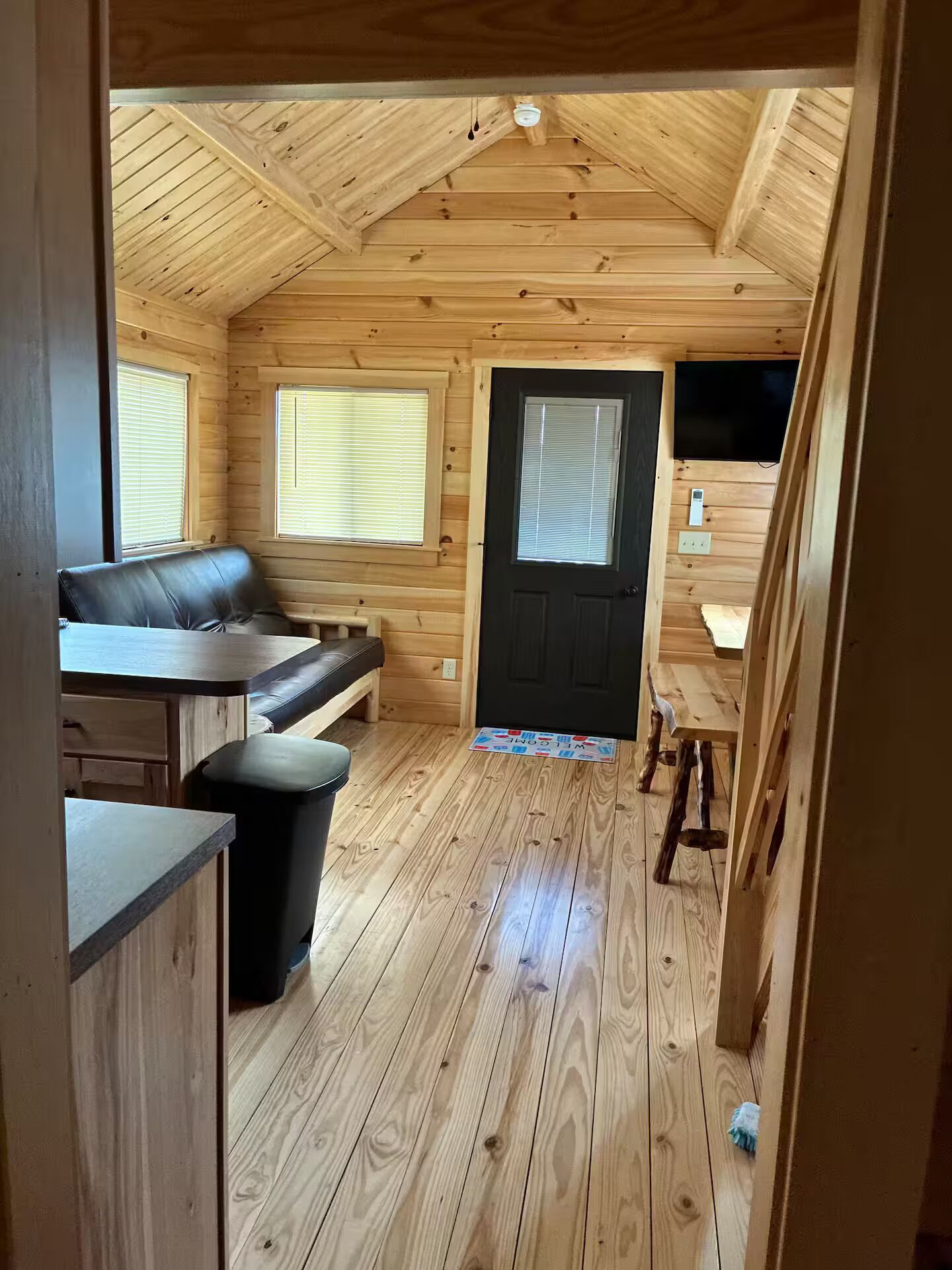 A cozy cabin interior with a wooden floor, a sofa, a dining table, and a black door.