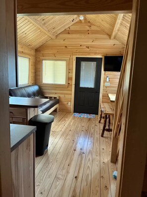A cozy cabin interior with a wooden floor, a sofa, a dining table, and a black door.