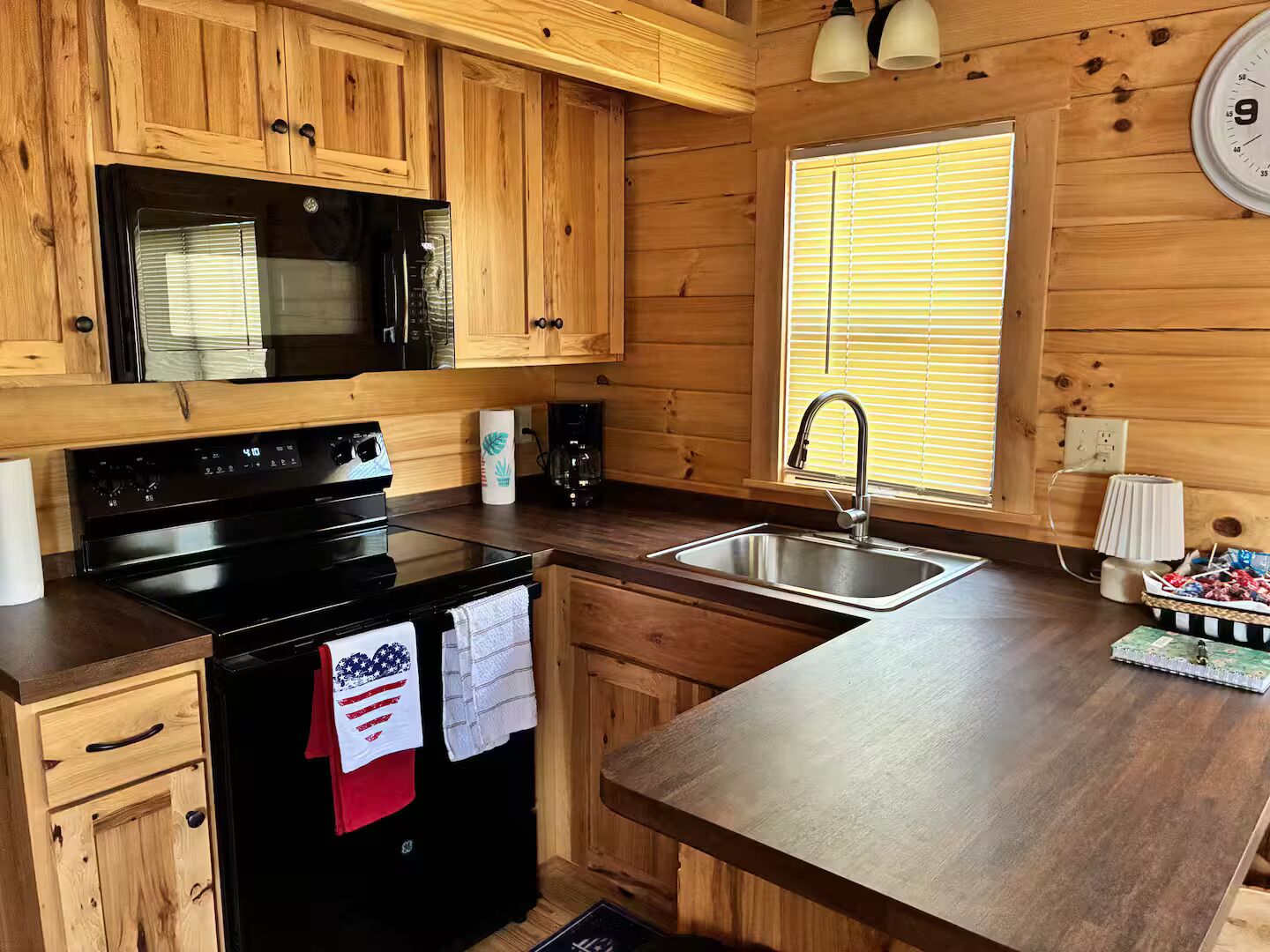 A kitchen with wooden cabinets, a black stove, a sink, and a window with blinds.