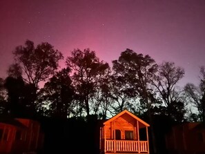 Een houten chalet met balkon, omringd door bomen, onder een sterrenhemel.