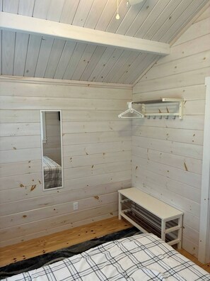A room with a bed, a bench, a mirror, and a hanging clothes rack.