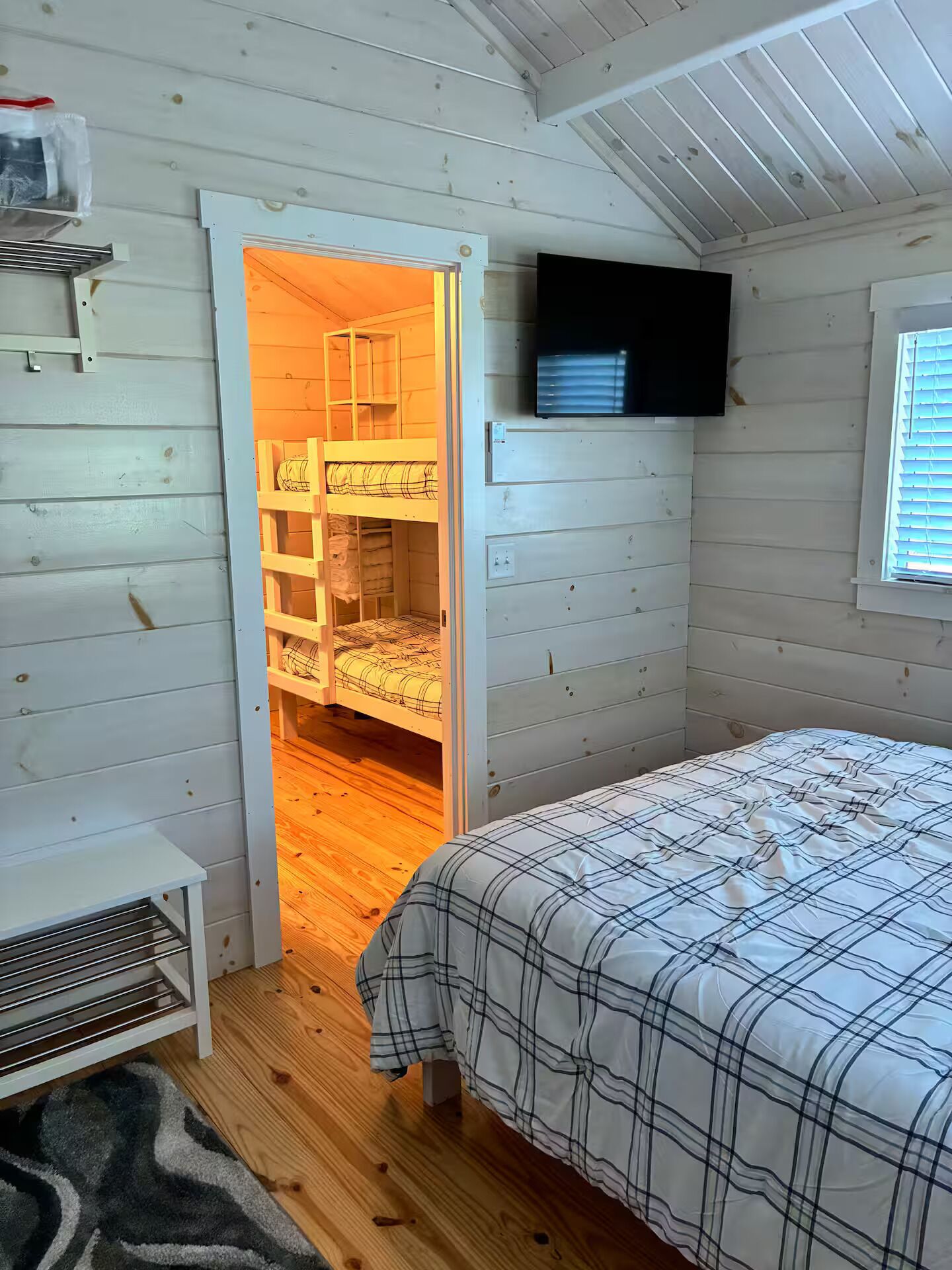 A bedroom with a bunk bed, a television mounted on the wall, and a window with blinds.