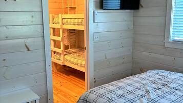 A bedroom with a bunk bed, a television mounted on the wall, and a window with blinds.