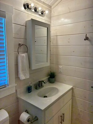 Een badkamer met een wit wastafelmeubel, een spiegel, een handdoekhouder, een kleine pot met een plantje en een toilet.